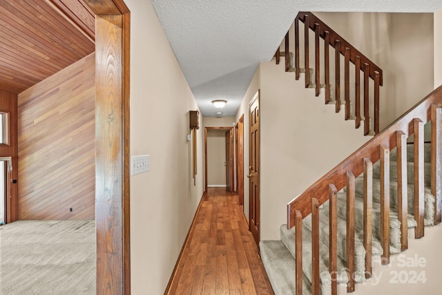 hall with light hardwood / wood-style flooring, wood walls, and a textured ceiling