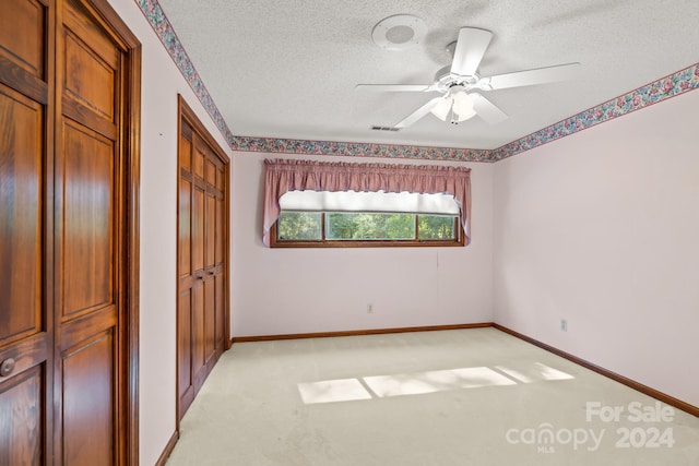 unfurnished bedroom featuring ceiling fan, light carpet, and a textured ceiling