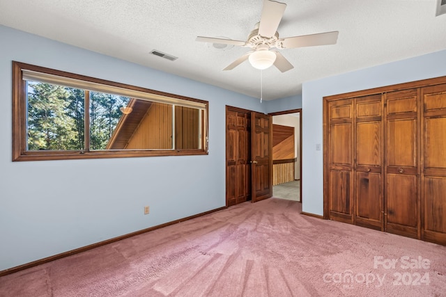 unfurnished bedroom with a textured ceiling, two closets, carpet flooring, and ceiling fan