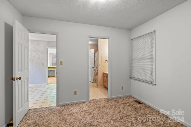 unfurnished bedroom featuring ensuite bath, light carpet, and a textured ceiling