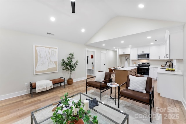 living room featuring sink, vaulted ceiling, and light wood-type flooring