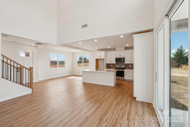 809 Terra Dr, Tega Cay, SC 29708 - unfurnished living room featuring stairway, baseboards, visible vents, a high ceiling, and light wood-style flooring