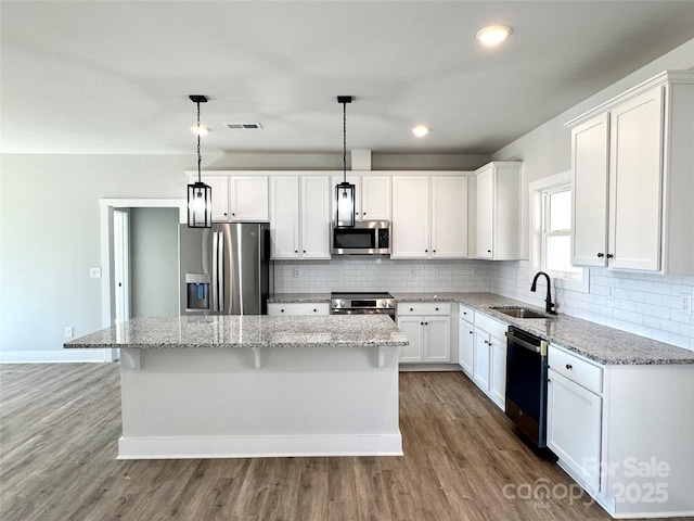 kitchen with hanging light fixtures, appliances with stainless steel finishes, sink, white cabinetry, and a center island