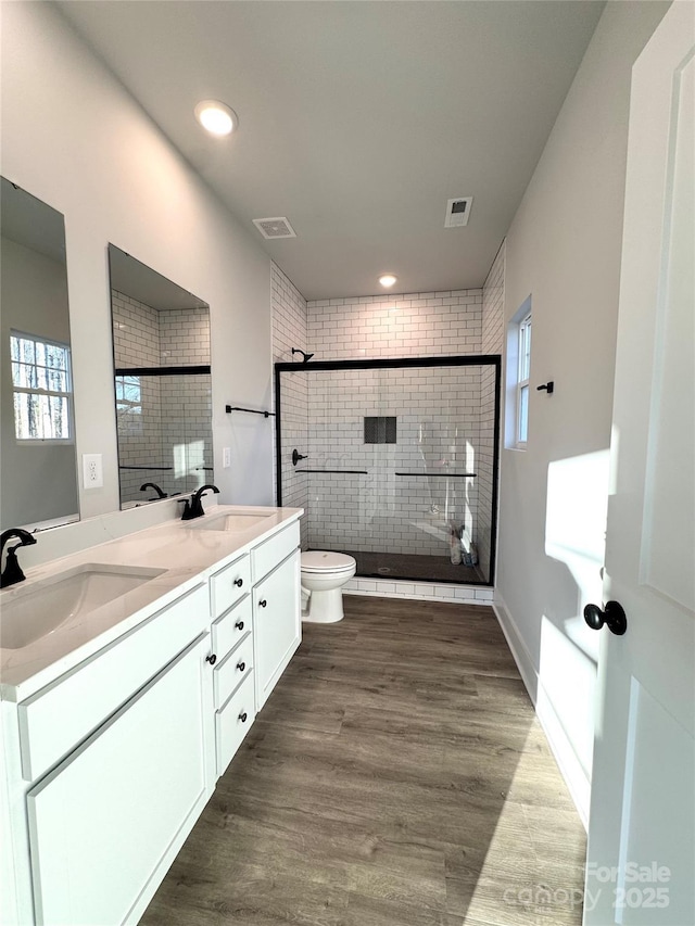 bathroom with hardwood / wood-style floors, toilet, vanity, and a tile shower