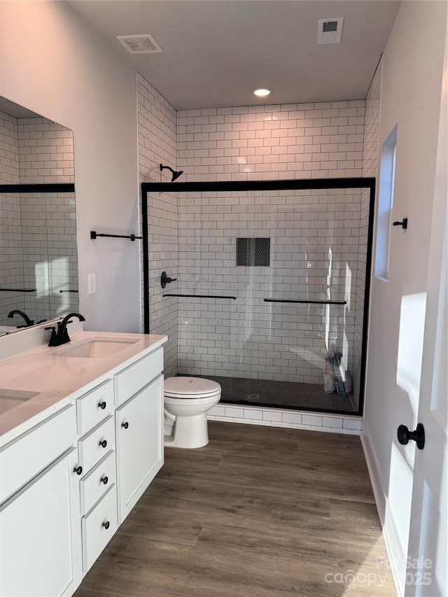 bathroom with hardwood / wood-style flooring, toilet, a shower with shower door, and vanity