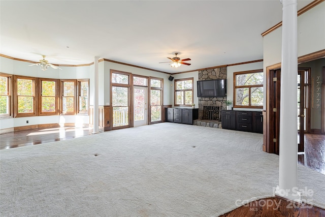 unfurnished living room with ceiling fan, a stone fireplace, carpet floors, and ornate columns