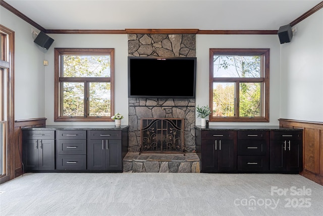 carpeted living room with crown molding, a stone fireplace, and a healthy amount of sunlight