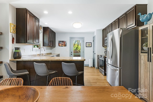 kitchen with a breakfast bar, sink, light hardwood / wood-style flooring, kitchen peninsula, and stainless steel appliances