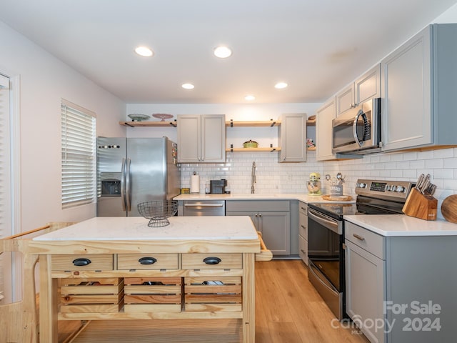 kitchen with tasteful backsplash, appliances with stainless steel finishes, sink, light wood-type flooring, and gray cabinets