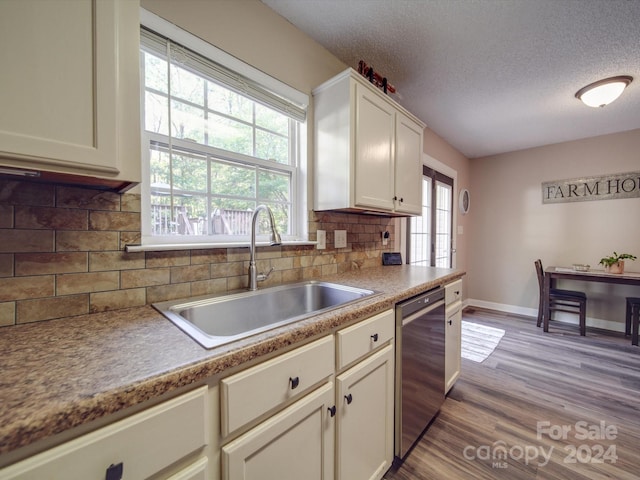 kitchen with sink, light wood-type flooring, a textured ceiling, stainless steel dishwasher, and decorative backsplash