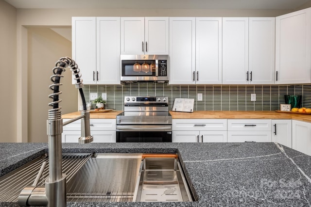 kitchen with appliances with stainless steel finishes, decorative backsplash, white cabinetry, and butcher block countertops