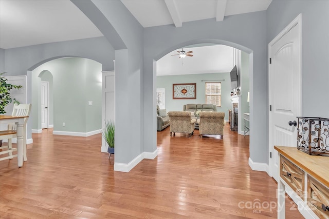 hall featuring beam ceiling, baseboards, light wood-type flooring, and arched walkways