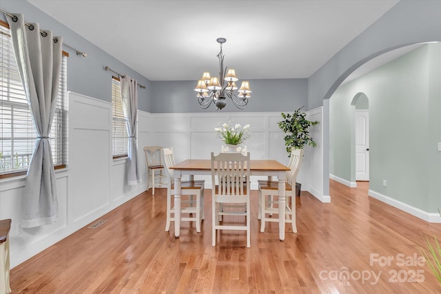 dining room with visible vents, arched walkways, light wood-style floors, and a chandelier