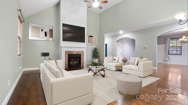 living room with arched walkways, a stone fireplace, a ceiling fan, and wood finished floors