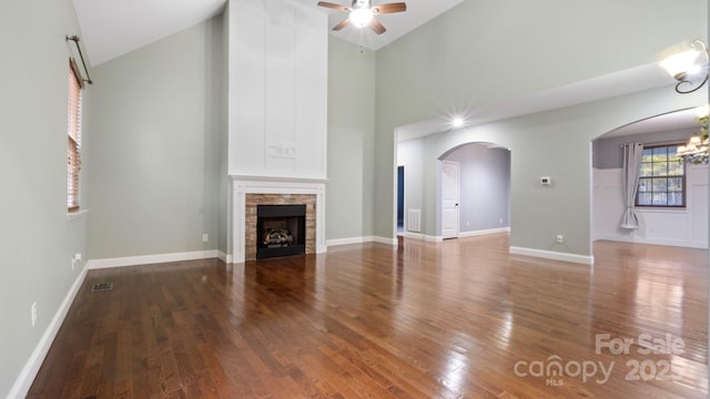 unfurnished living room with hardwood / wood-style flooring, a stone fireplace, ceiling fan with notable chandelier, and high vaulted ceiling