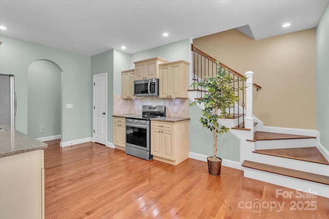 kitchen featuring appliances with stainless steel finishes, tasteful backsplash, light stone counters, cream cabinetry, and light hardwood / wood-style flooring