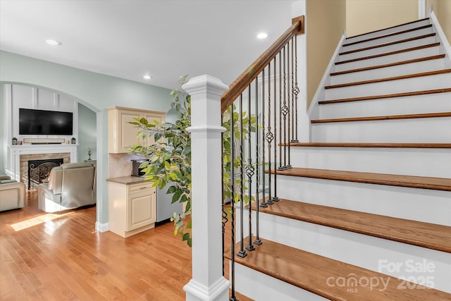 stairs featuring wood finished floors, recessed lighting, a fireplace, and arched walkways