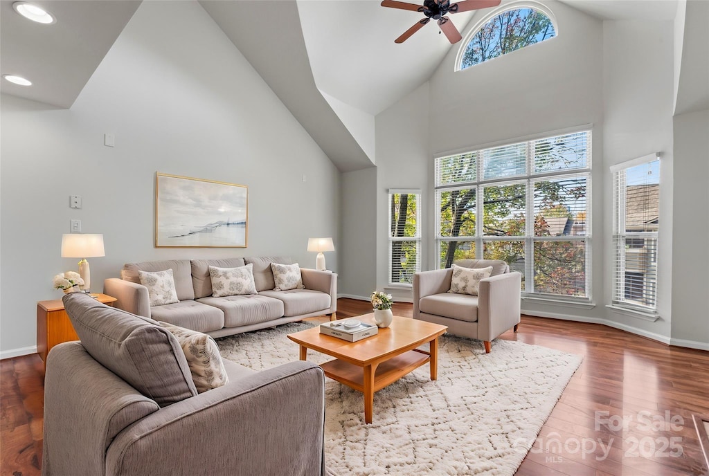 living room with ceiling fan, a towering ceiling, and hardwood / wood-style flooring