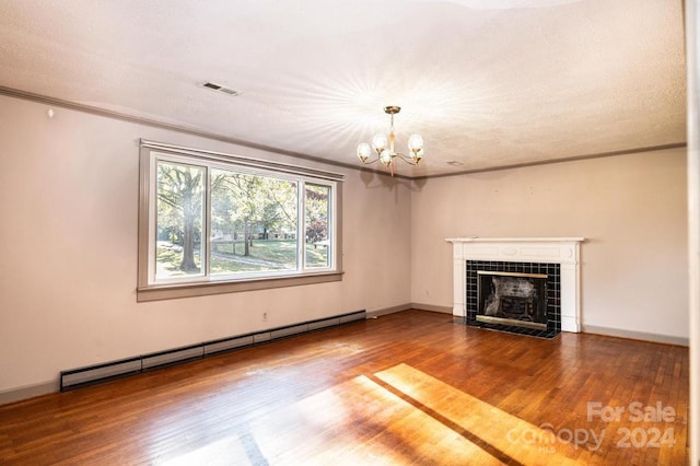 unfurnished living room with a baseboard heating unit, a tiled fireplace, hardwood / wood-style floors, a textured ceiling, and a notable chandelier