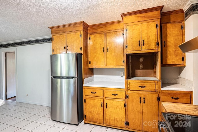 kitchen with crown molding, stainless steel fridge, light tile patterned flooring, and a textured ceiling