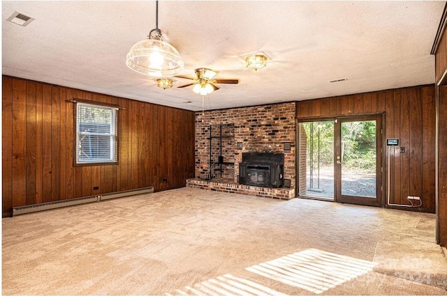 unfurnished living room featuring a baseboard radiator, wooden walls, a healthy amount of sunlight, and a wood stove