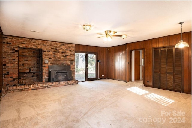 unfurnished living room featuring light colored carpet, a wood stove, wooden walls, and ceiling fan