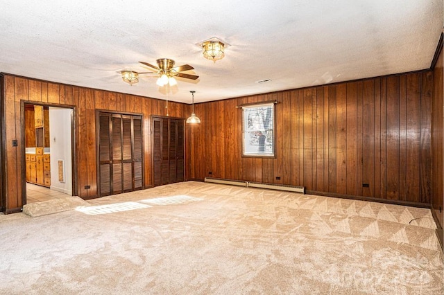 carpeted spare room with ceiling fan, a textured ceiling, a baseboard heating unit, and wooden walls