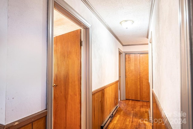 hallway with wood walls, wood-type flooring, a baseboard radiator, a textured ceiling, and crown molding