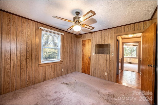 carpeted empty room featuring crown molding, ceiling fan, a textured ceiling, and wood walls