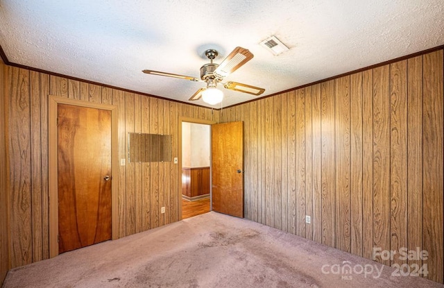 carpeted spare room featuring ceiling fan, a textured ceiling, ornamental molding, and wooden walls