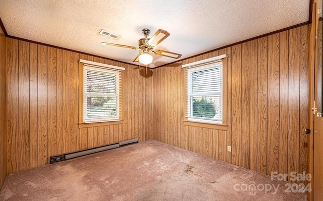 carpeted spare room featuring ceiling fan, a textured ceiling, a baseboard heating unit, and wooden walls