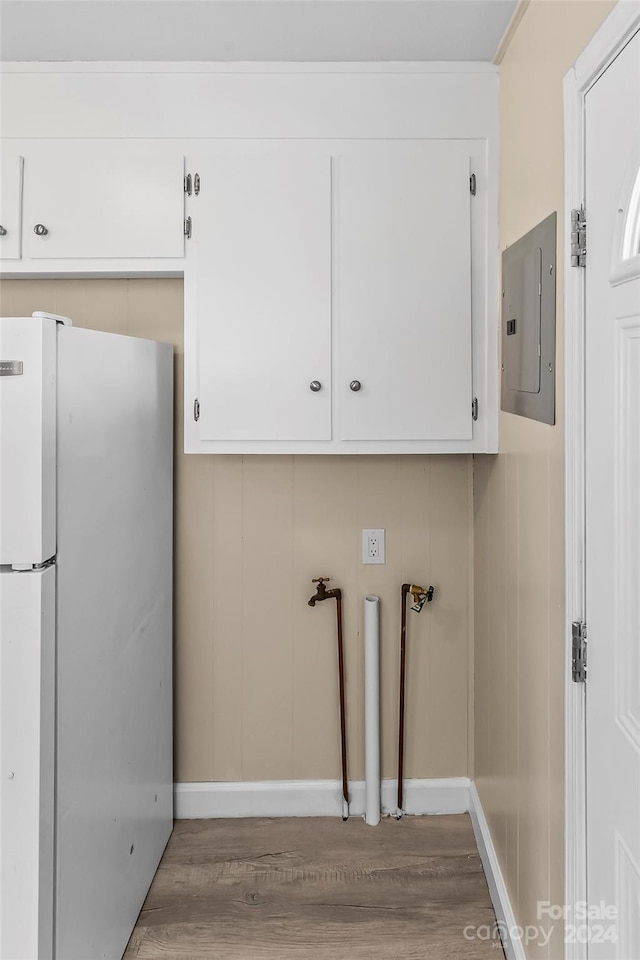 laundry area featuring electric panel, hardwood / wood-style flooring, and cabinets