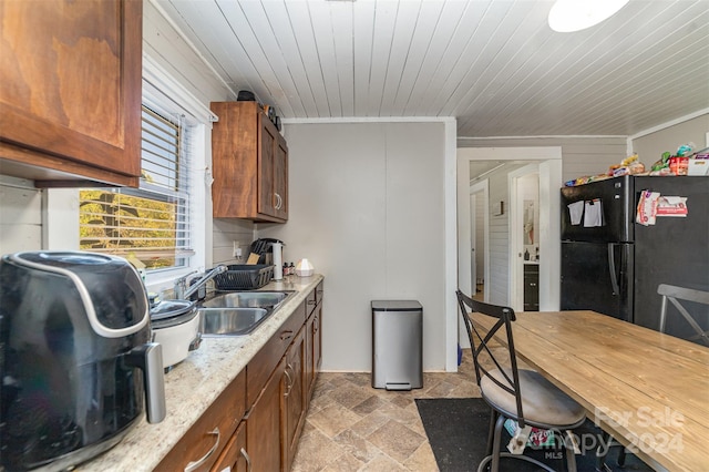 kitchen with wood walls, sink, wood ceiling, black fridge, and ornamental molding