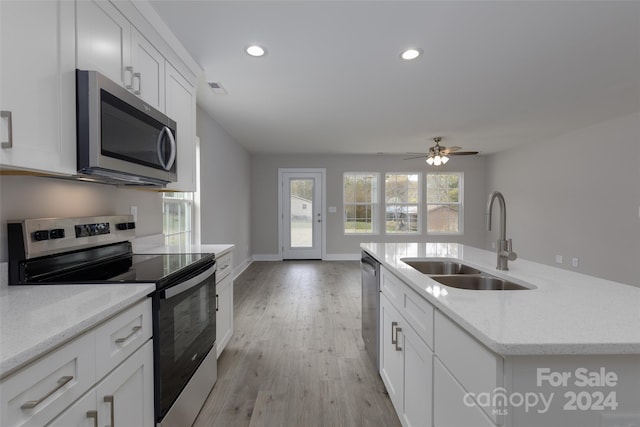 kitchen with a kitchen island with sink, stainless steel appliances, white cabinetry, sink, and light hardwood / wood-style flooring