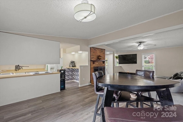 dining space featuring ceiling fan, sink, a brick fireplace, wood-type flooring, and a textured ceiling