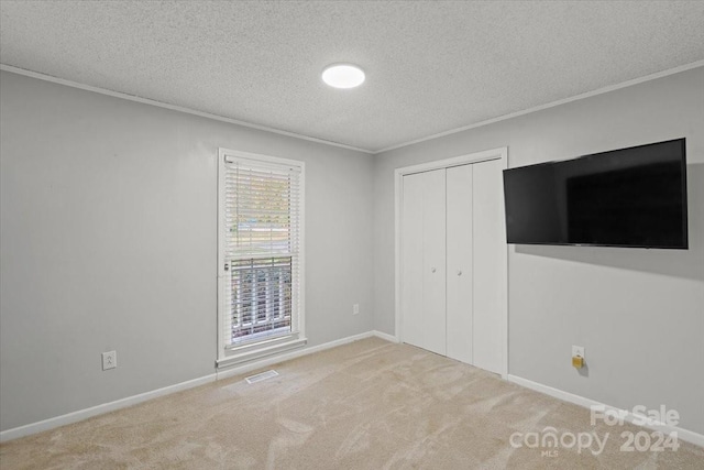 unfurnished bedroom with light carpet, a closet, crown molding, and a textured ceiling