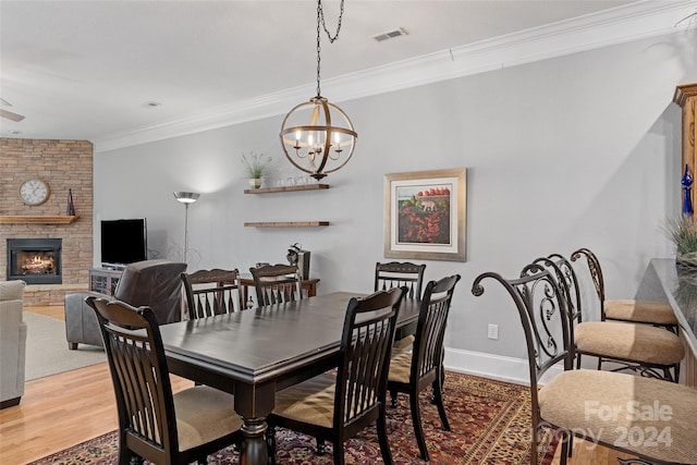 dining space featuring a stone fireplace, an inviting chandelier, hardwood / wood-style flooring, and crown molding