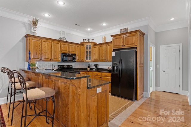 kitchen with kitchen peninsula, tasteful backsplash, a kitchen breakfast bar, black appliances, and crown molding