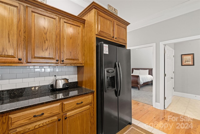 kitchen with ornamental molding, stainless steel fridge, dark stone counters, and light hardwood / wood-style floors