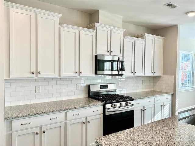 kitchen with white cabinets, decorative backsplash, light stone counters, and stainless steel appliances