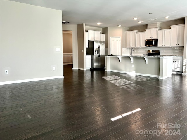 kitchen featuring a kitchen bar, stainless steel appliances, a center island with sink, white cabinets, and dark hardwood / wood-style floors