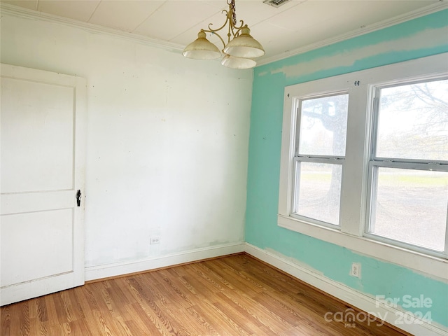 empty room featuring hardwood / wood-style flooring, crown molding, and a chandelier