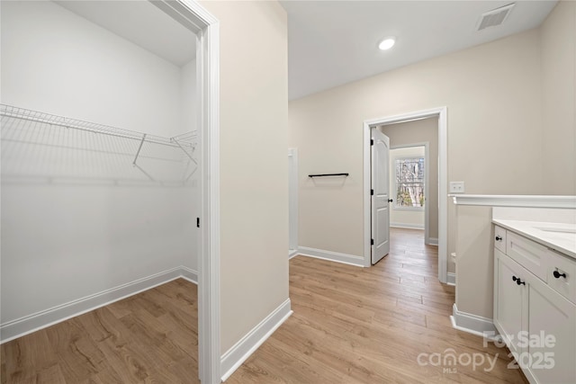 bathroom with baseboards, wood finished floors, visible vents, and a walk in closet