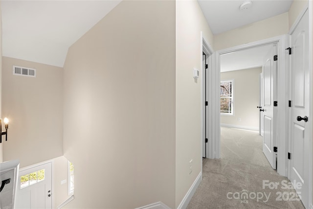 hallway with baseboards, visible vents, vaulted ceiling, and light colored carpet