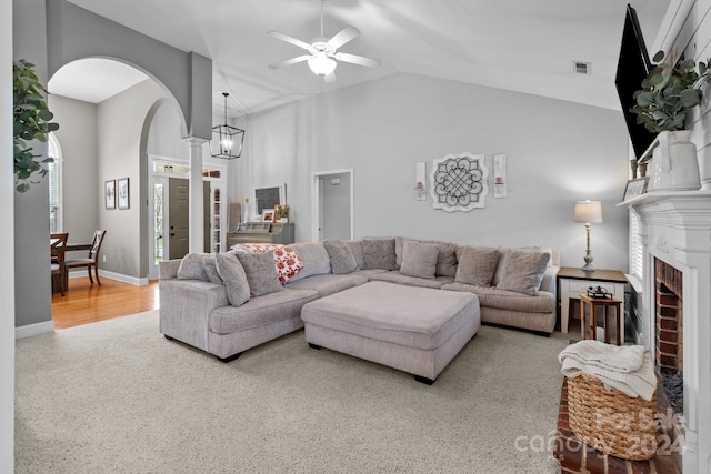 carpeted living room with a fireplace, ceiling fan, and high vaulted ceiling