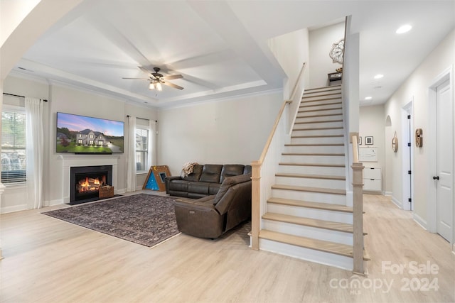 living room featuring light hardwood / wood-style floors, a raised ceiling, ornamental molding, and ceiling fan