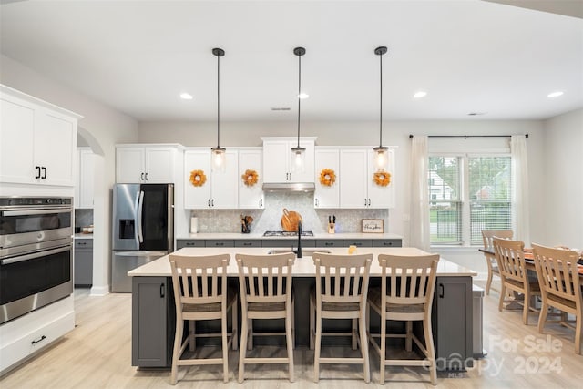 kitchen featuring appliances with stainless steel finishes, white cabinetry, hanging light fixtures, and an island with sink