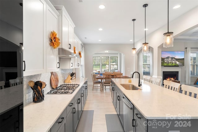 kitchen featuring white cabinets, a center island with sink, appliances with stainless steel finishes, pendant lighting, and sink