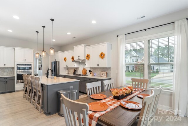 kitchen featuring white cabinets, decorative light fixtures, a center island with sink, and gray cabinetry