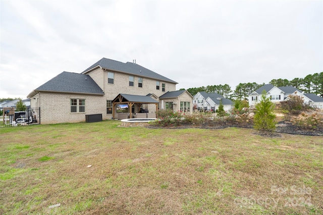 back of property with a hot tub, a patio, and a lawn